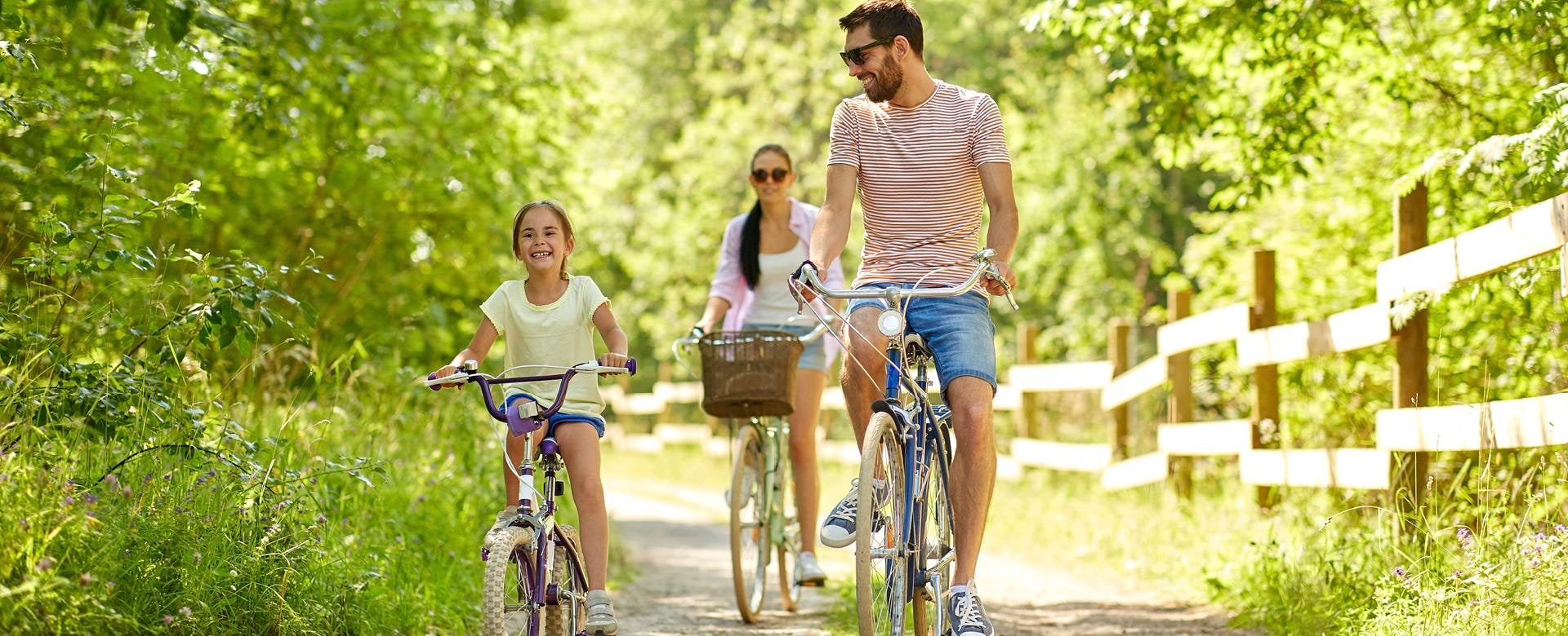 Familien-, Freizeit- und People-Konzept - glückliche Mutter, Vater und kleine Tochter reiten Fahrräder im Sommerpark
